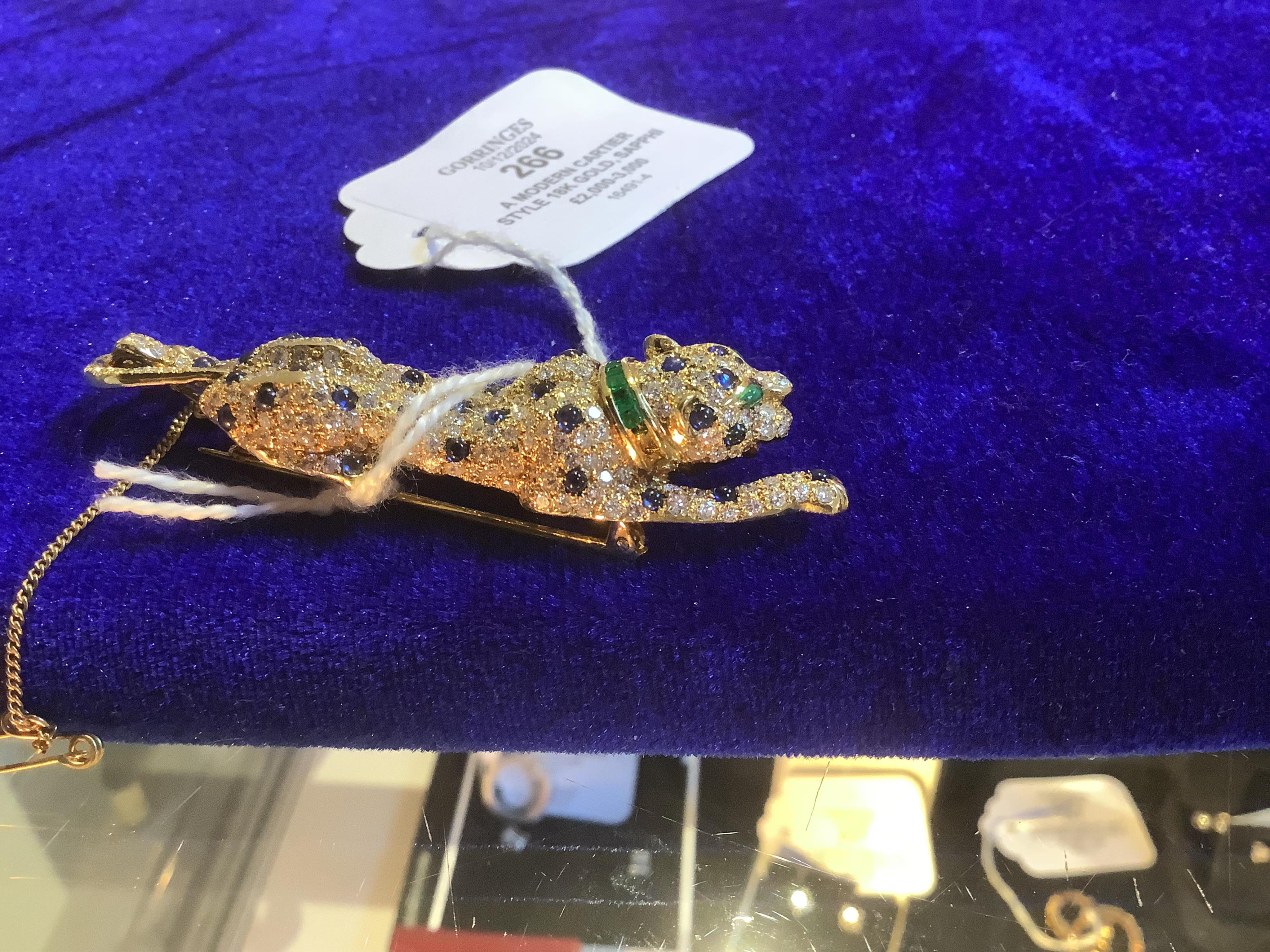 A modern Cartier style 18k gold, sapphire, emerald and diamond cluster set stalking panther brooch